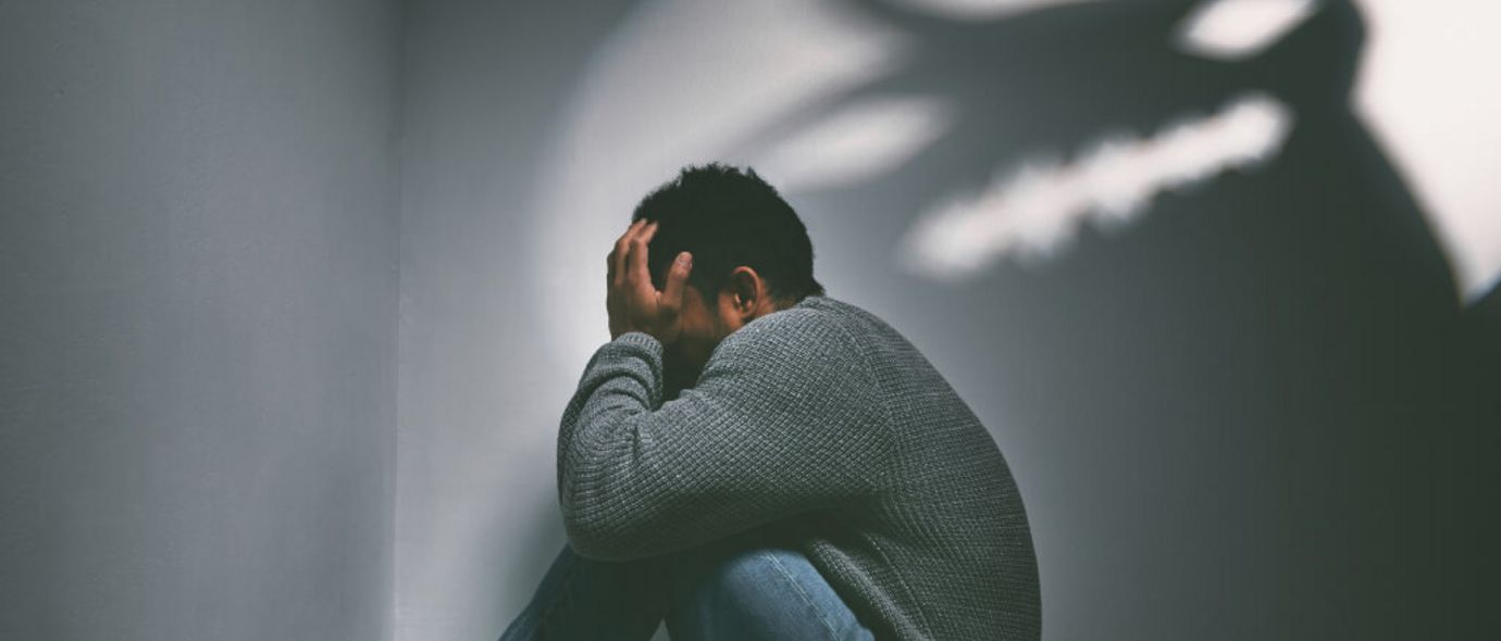 Mann sitzt in Zimmerecke mit gruseliger alptraumhafter Figur an der Wand im Hintergrund