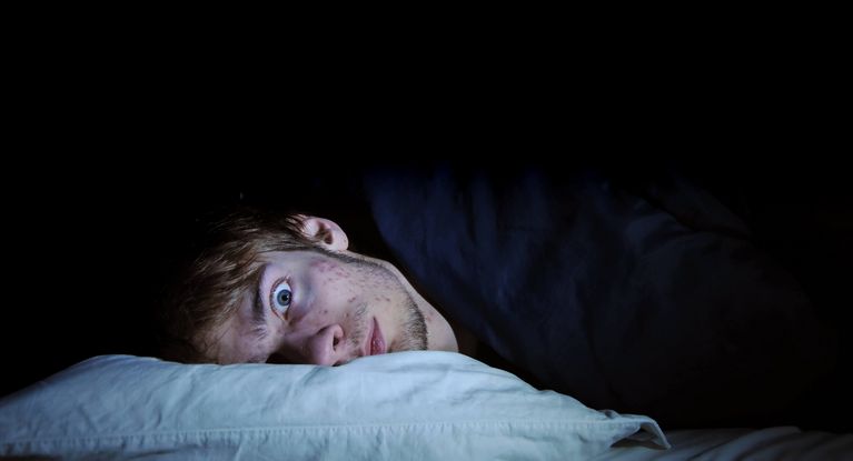 Schlafloser Mann liegt nachts mit offenen Augen auf einem Kissen