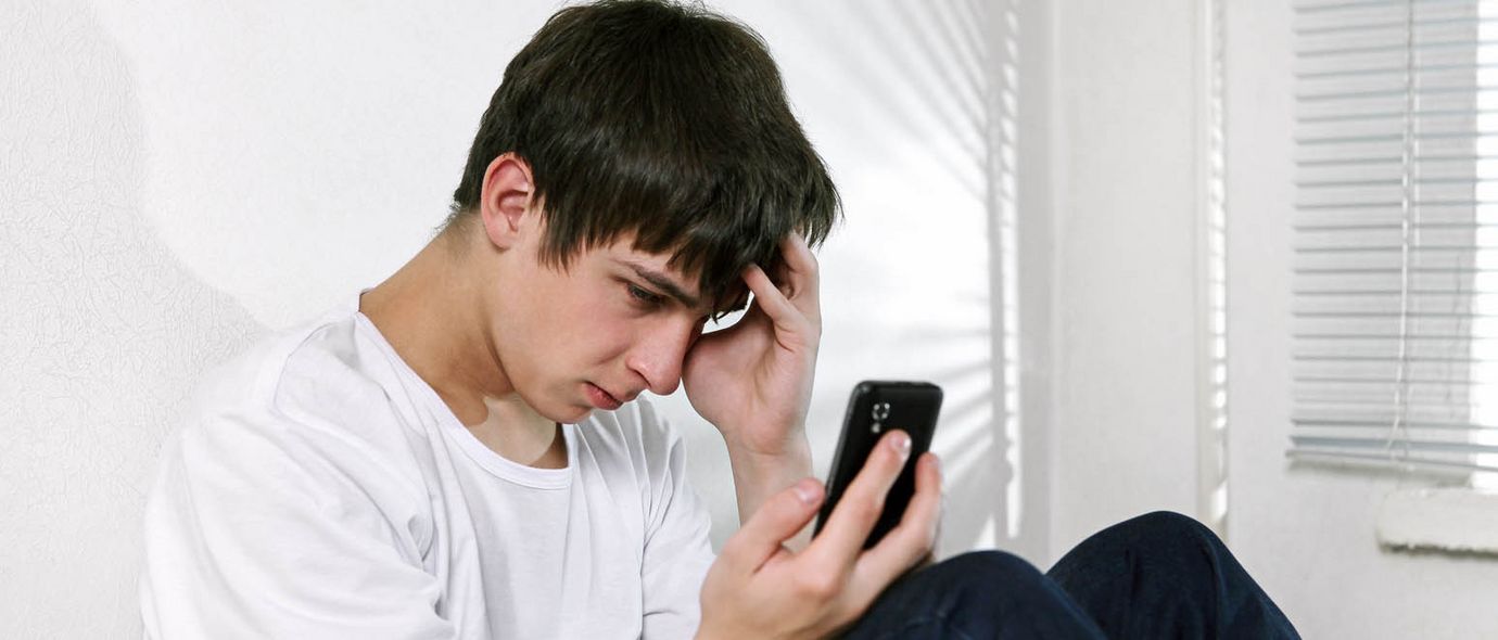 Trauriger junger Mann schaut auf sein Smartphone